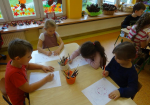 Czworo dzieci siedzi przy stoliku, w ręku trzymają kredki, którymi poprawiają po śladzie wykropkowane zegary.